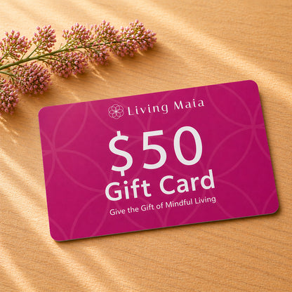 Living Maia $50 gift card on wooden surface with soft light and pink flowers