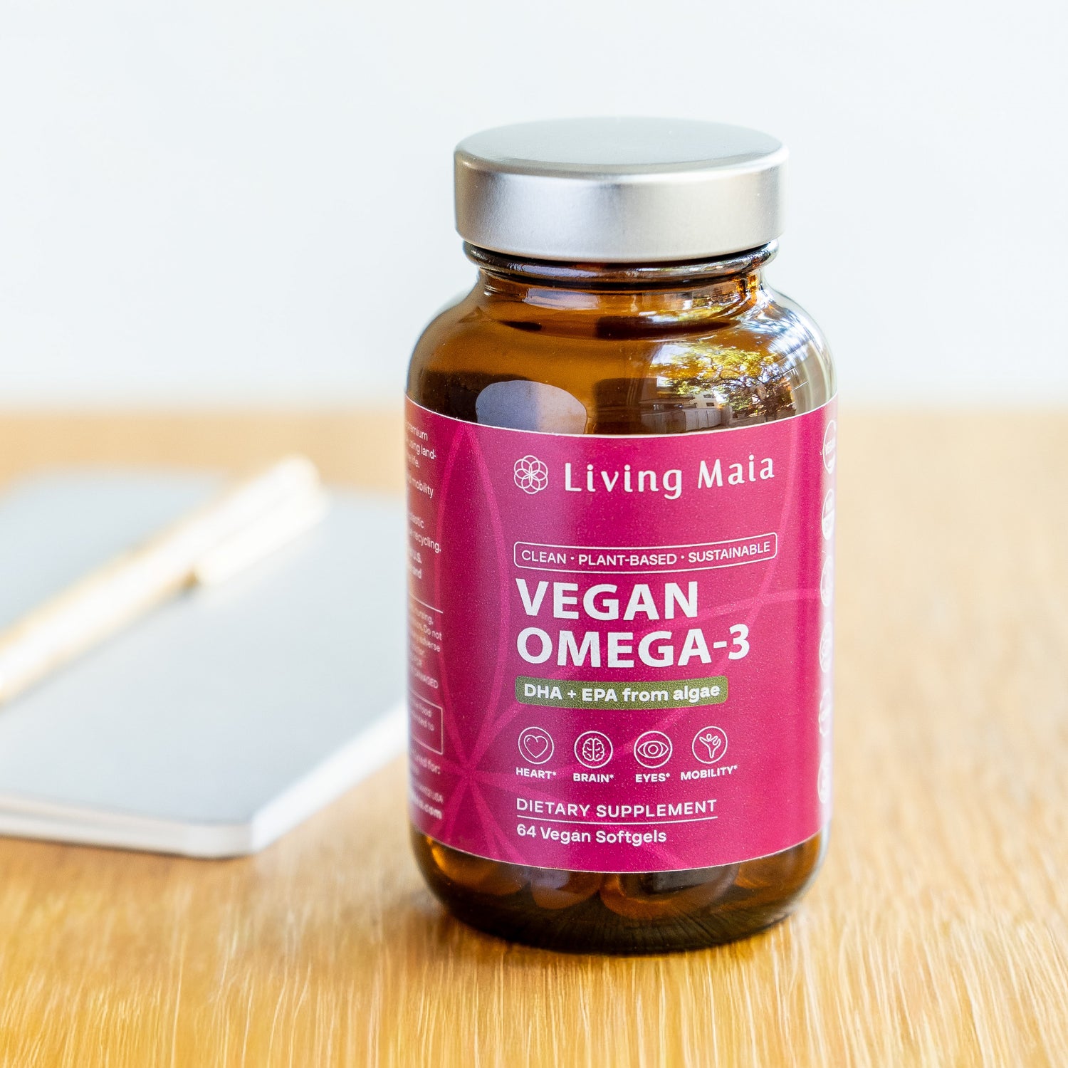 Living Maia vegan Omega-3 supplement bottle on desk with notebook and pen
